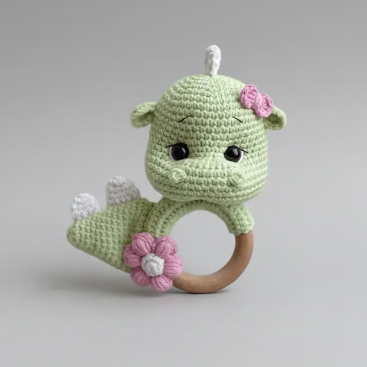 Crocheted green dinosaur baby rattle with pink flowers on wooden ring