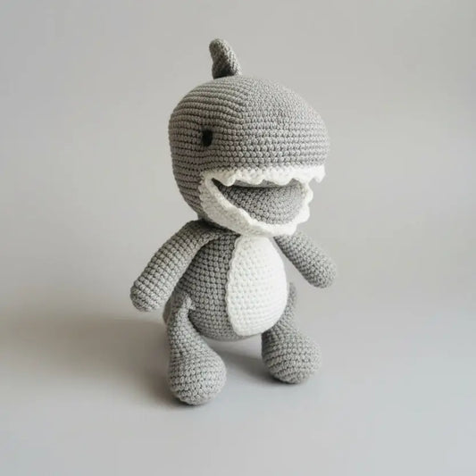 Crocheted gray shark plush toy with white belly, sitting upright on plain background
