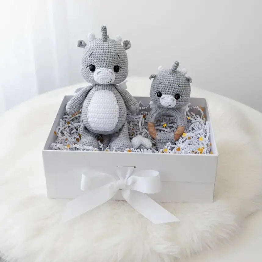 Two crocheted gray rhinos in a white gift box with ribbon, nestled on shredded paper