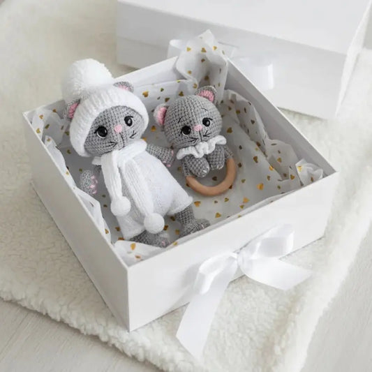 Two crocheted gray and white stuffed animal cats in a white gift box with golden hearts