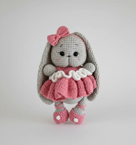 Crocheted gray bunny with pink bow and ruffled dress, standing on white background