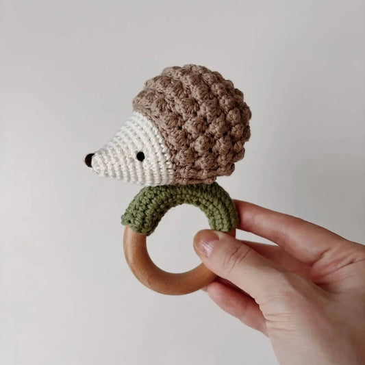 Crocheted hedgehog baby rattle with wooden teething ring, held by a hand