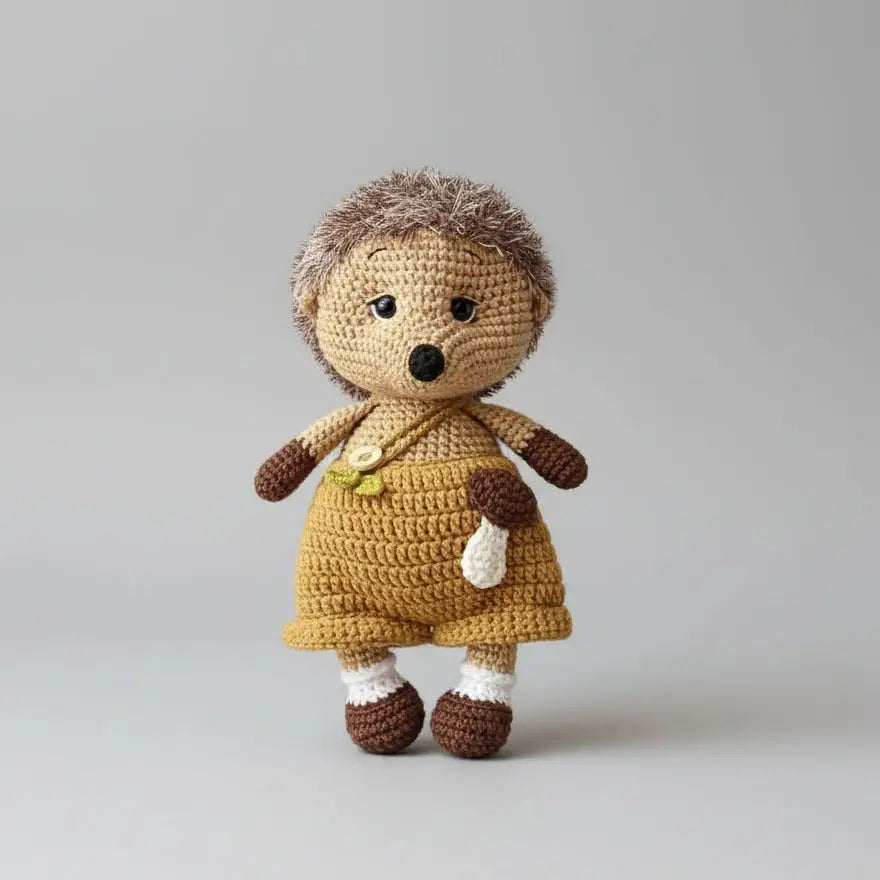 Crocheted hedgehog doll in yellow dress with brown trim, standing on gray background