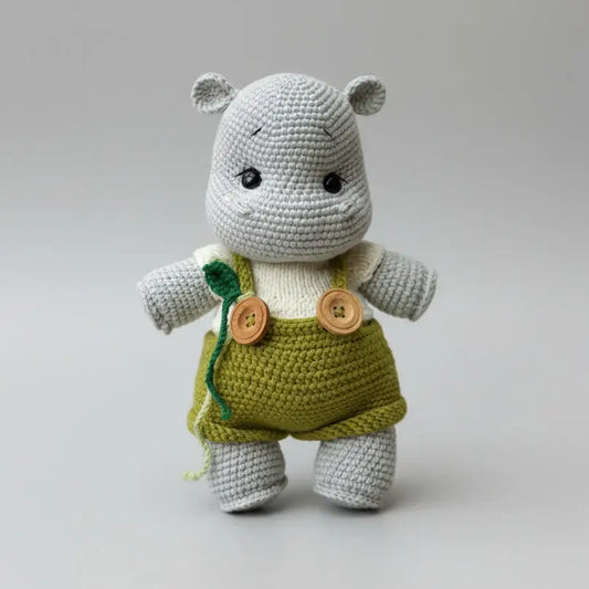 Crocheted gray hippo wearing green overalls with wooden buttons on neutral background