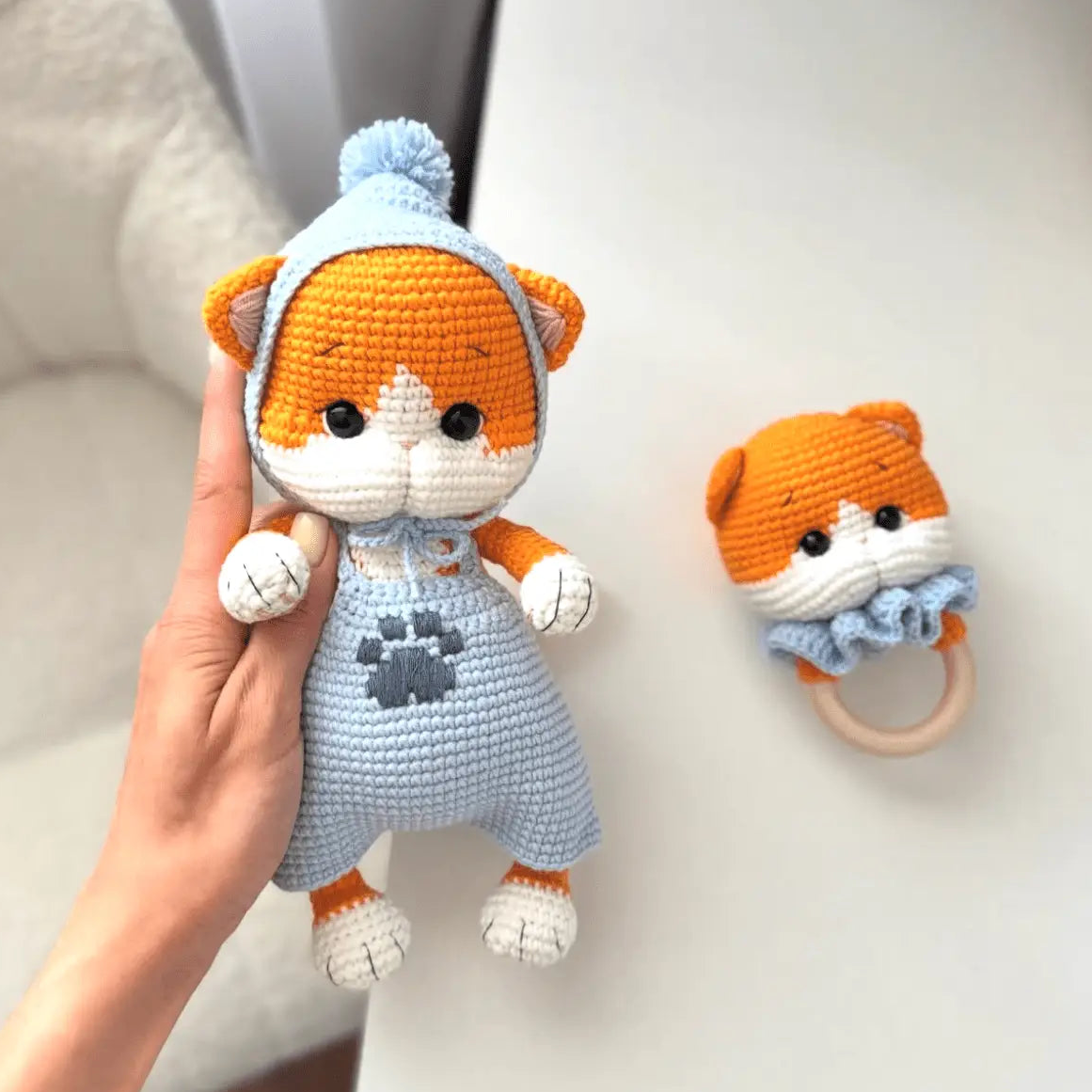 Crocheted orange and white cat doll in blue outfit with matching small rattle toy