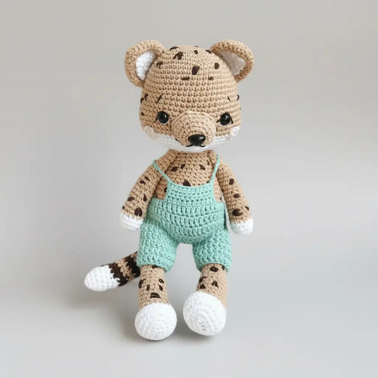 Crocheted leopard-like stuffed animal wearing mint green overalls on gray background