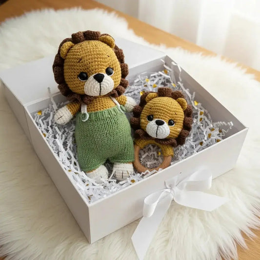 Two crocheted lion stuffed animals in a white gift box with white ribbon, sitting on fluffy white surface