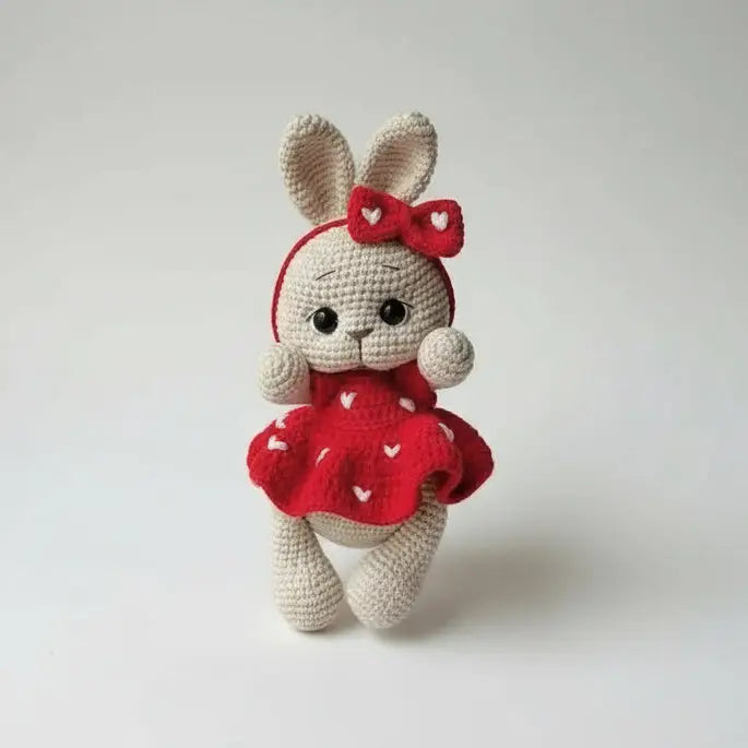 Crocheted bunny in red dress with bow, standing against neutral background
