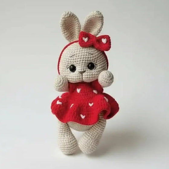 Crocheted bunny in red dress with bow, standing against neutral background