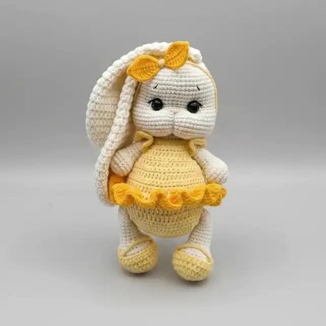 Crocheted white bunny with yellow dress and accents, standing on gray background