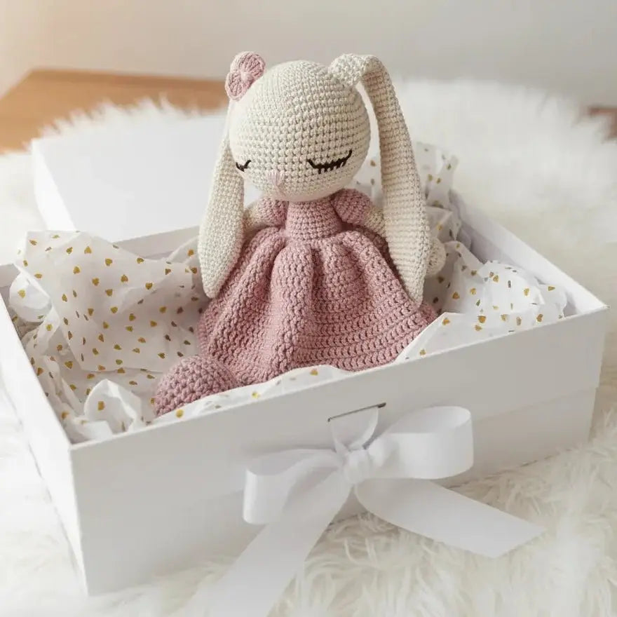 Crocheted bunny in pink dress nestled in white gift box with gold heart pattern