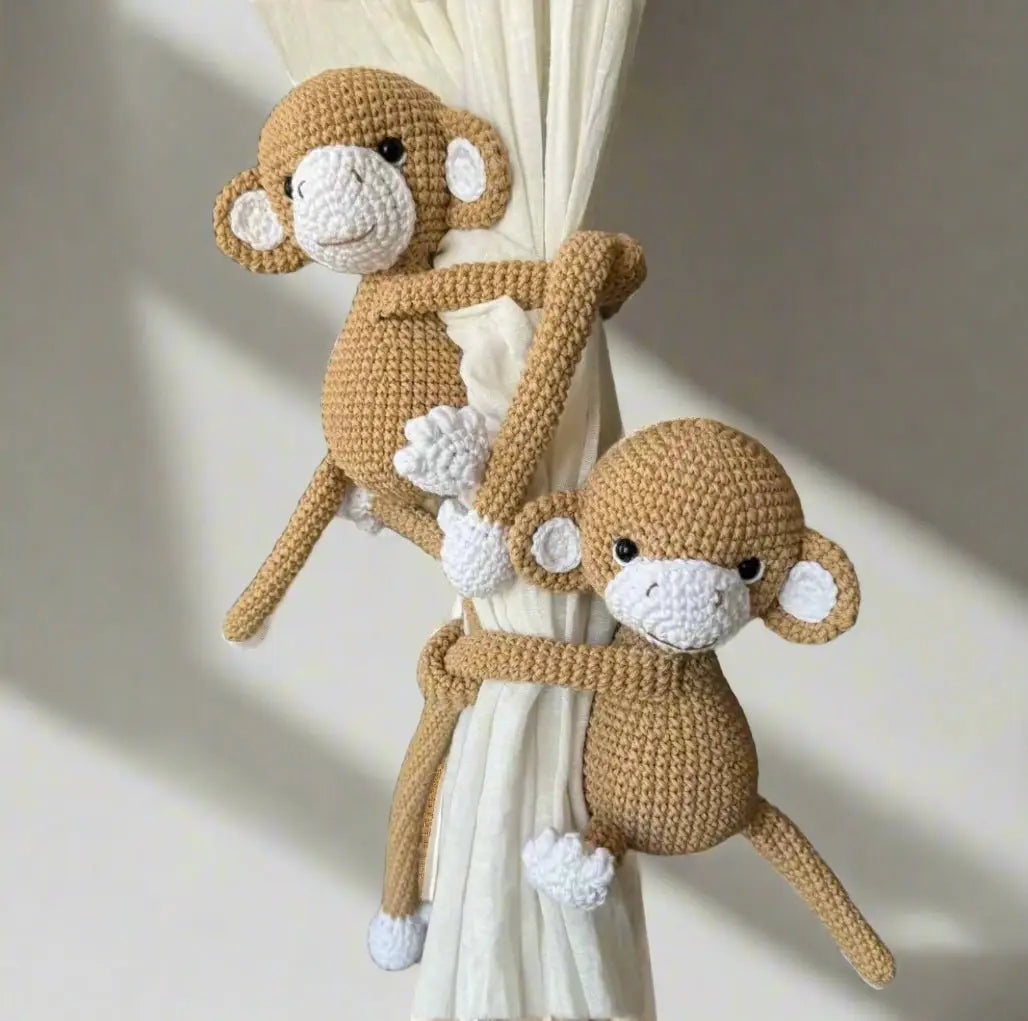 Two crocheted monkeys hugging a white curtain with adorable round shapes and white accents.