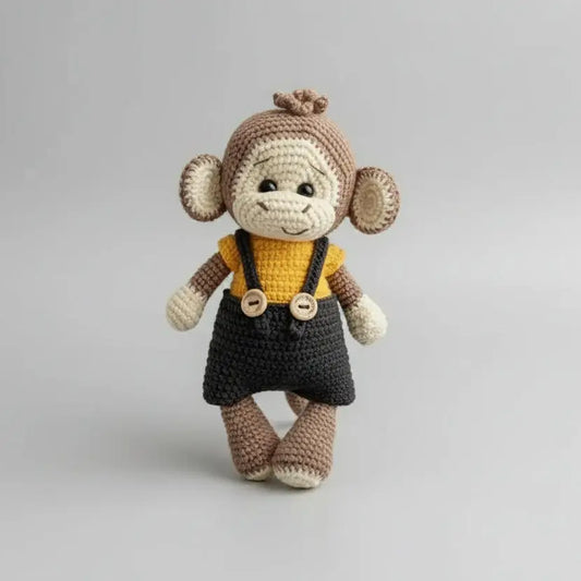 Crocheted monkey in yellow shirt and black overalls, standing against gray background