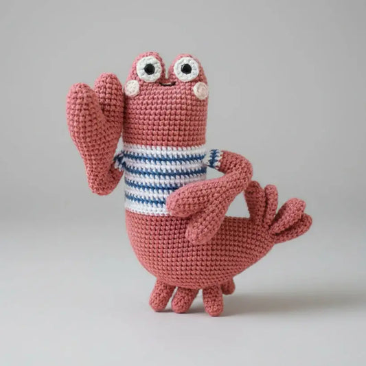 Pink crocheted creature with googly eyes and blue-white striped shirt on gray background