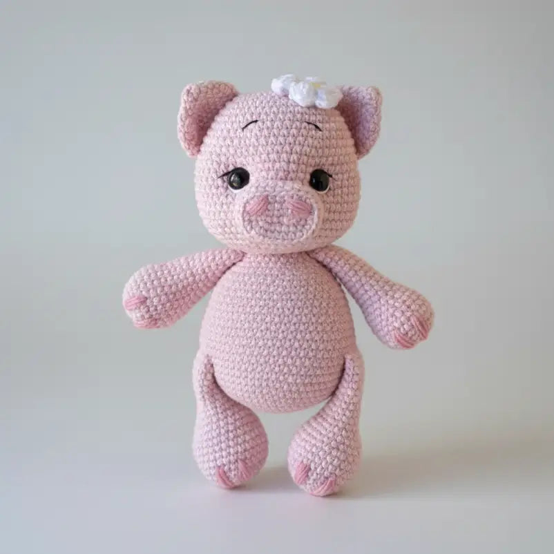 Pink crocheted pig stuffed animal with a white flower on its ear