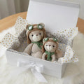 Two crocheted teddy bears in pilot hats and scarves nestled in a white gift box with gold-dotted tissue paper.