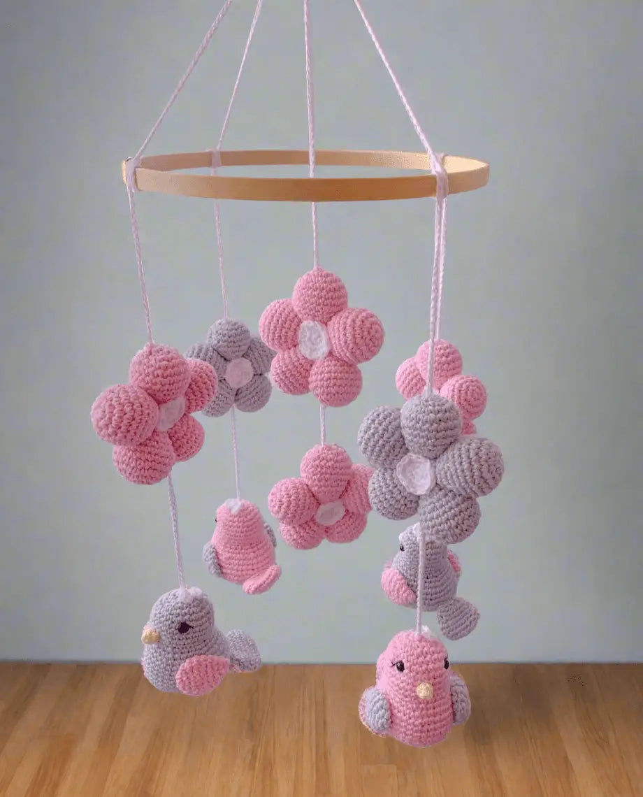 Crocheted baby mobile with pink and gray birds, flowers, and hanging spheres on wooden ring
