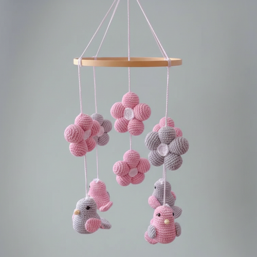 Crocheted baby mobile with pink and gray birds, flowers, and hanging spheres on wooden ring