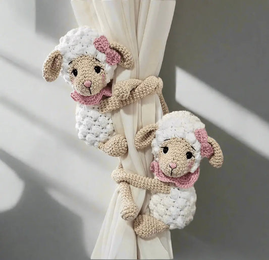 Two crocheted lamb curtain tie-backs with pink bows, hugging a white curtain.