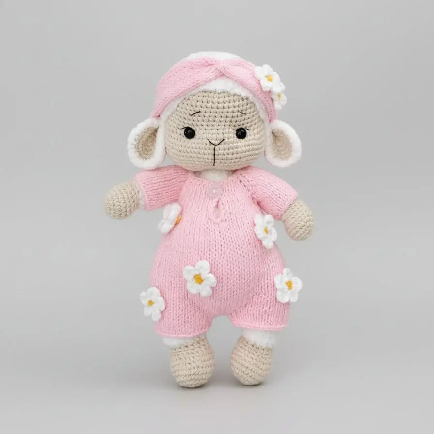 Crocheted lamb in pink outfit with white flower details, standing on neutral background
