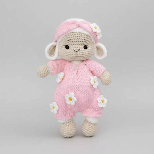 Crocheted lamb in pink outfit with white flower details, standing on neutral background