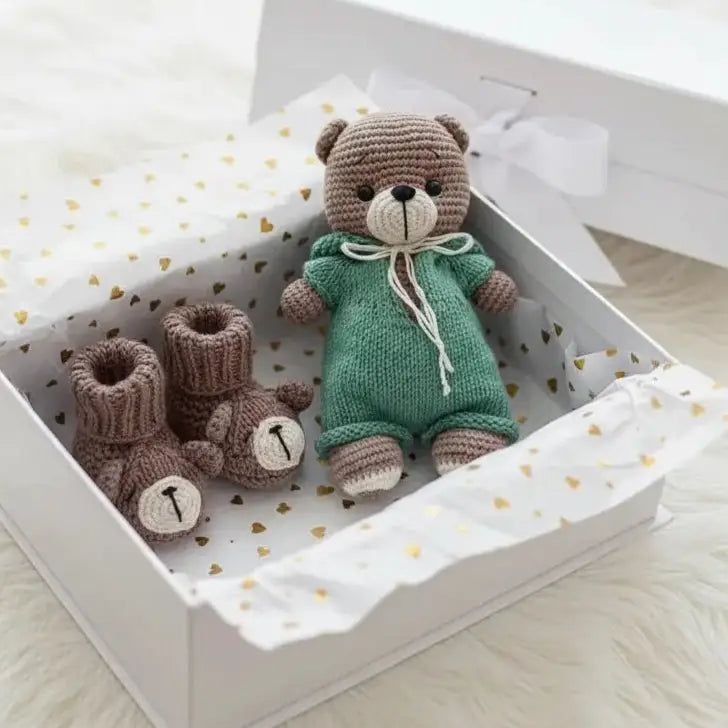 Crocheted teddy bear in green outfit with matching booties in a gift box with gold hearts