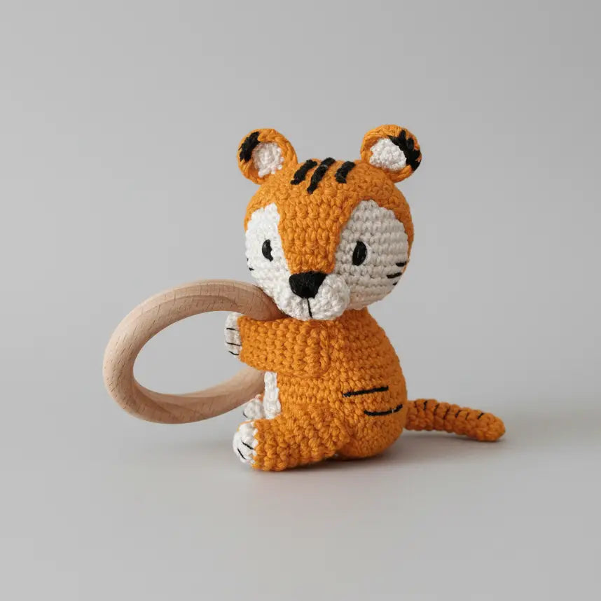 Crocheted orange tiger toy with wooden teething ring on gray background