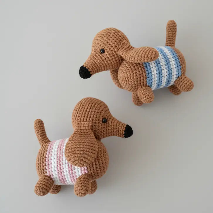 Two crocheted dachshund dogs with striped sweaters, sitting side by side on a gray background.