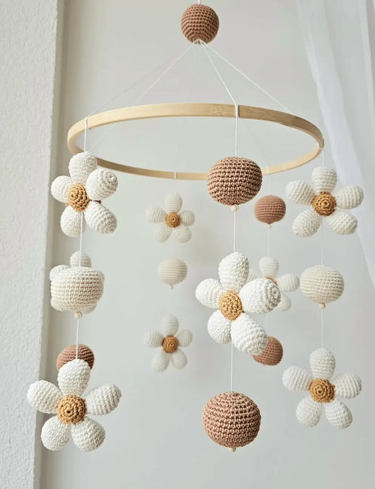Crocheted baby mobile with white and brown spheres and daisy-like flowers hanging from wooden ring