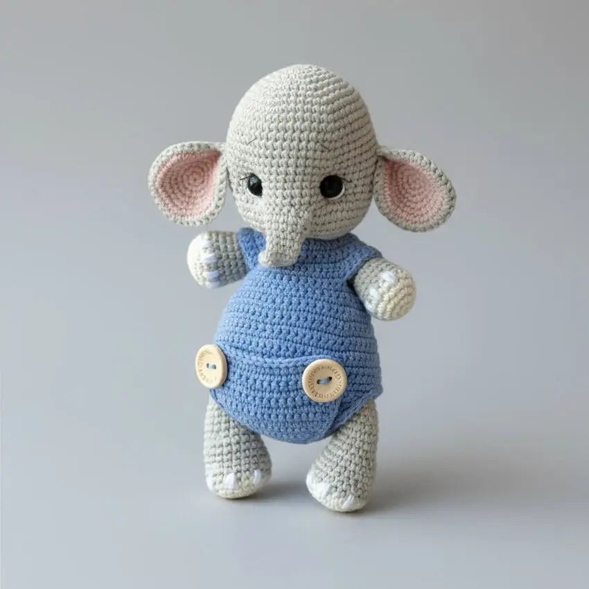 Crocheted elephant toy in blue overalls with wooden buttons on gray background