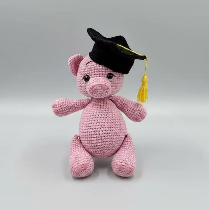 Pink crocheted pig wearing a black graduation cap with yellow tassel