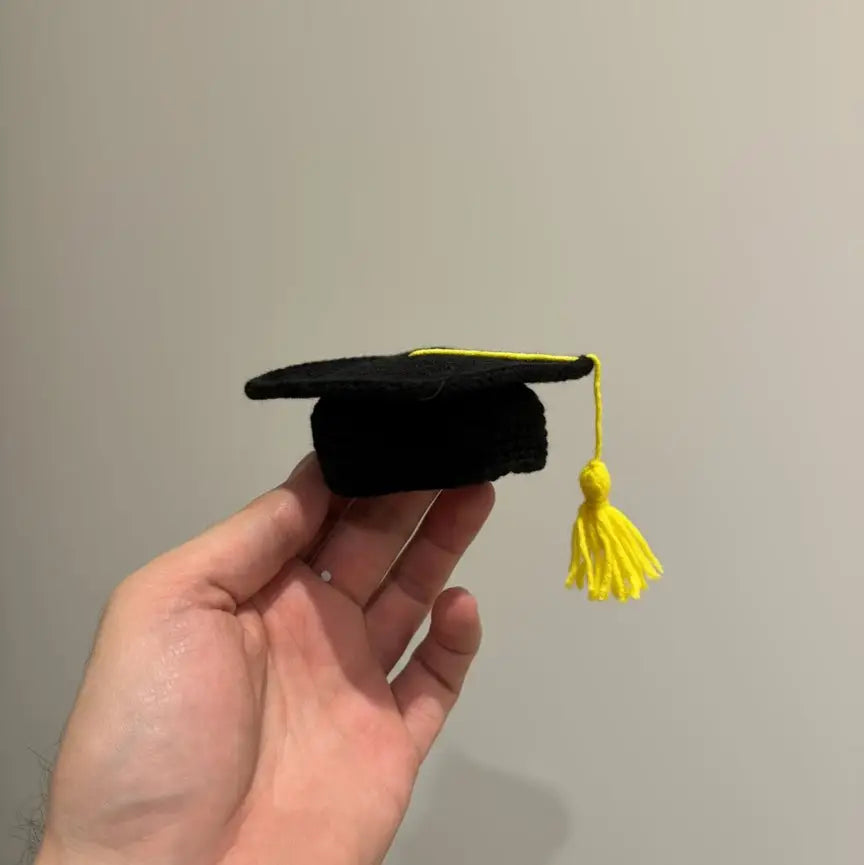 Black graduation cap with bright yellow tassel held in an open palm