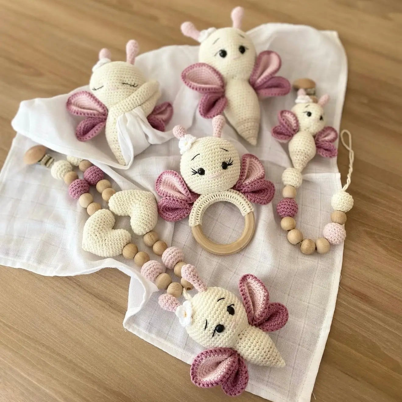 Crocheted butterfly-shaped baby toys in cream and pink, with wooden teething ring