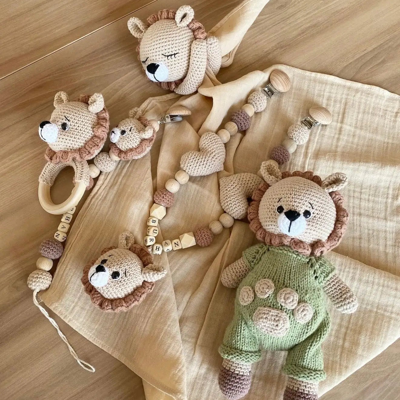 Handmade crocheted lion baby toys and accessories in neutral colors on wooden surface