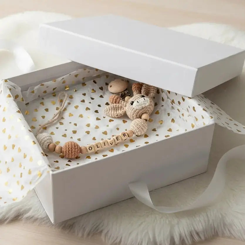 Handmade crochet baby toys and personalized name blocks in a white gift box with golden hearts