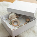 Crocheted sheep rattle and wooden beads in a white box on a fluffy white surface.