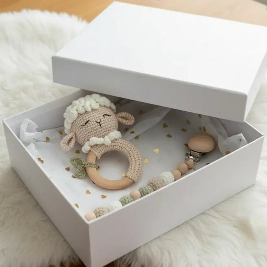 Crocheted sheep rattle and wooden beads in a white box on a fluffy white surface.