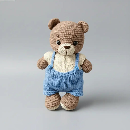Crocheted teddy bear in blue overalls standing against a gray background
