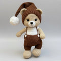 Crocheted teddy bear in brown overalls and nightcap with white pompom
