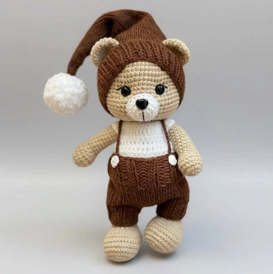 Crocheted teddy bear in brown overalls and nightcap with white pompom