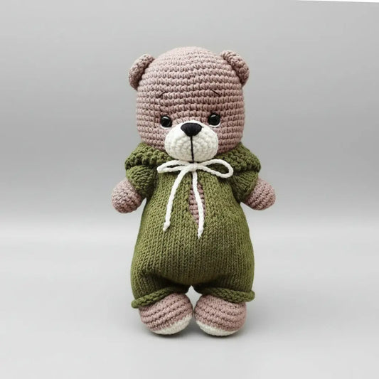 Crocheted teddy bear in olive green overalls with white bow tie, sitting sweetly
