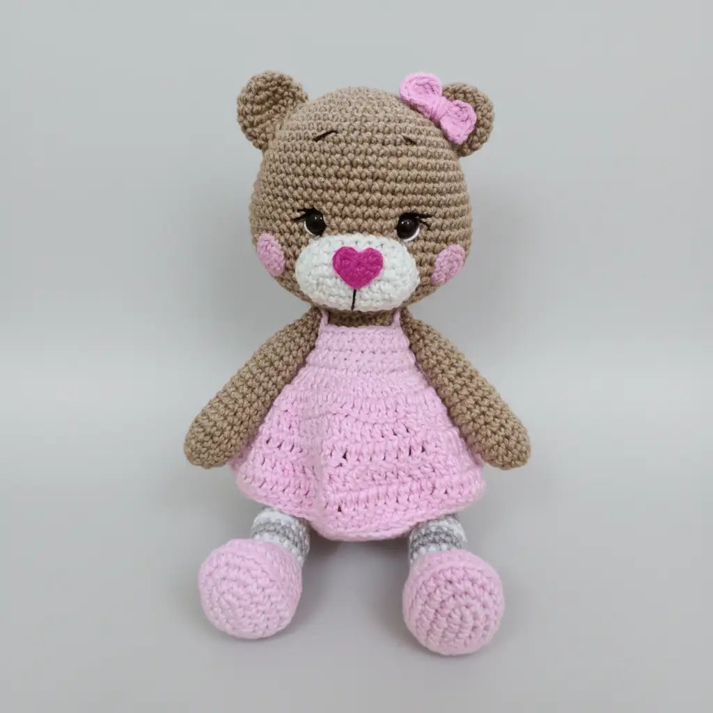 Crocheted teddy bear with pink dress, bow, and heart-shaped nose