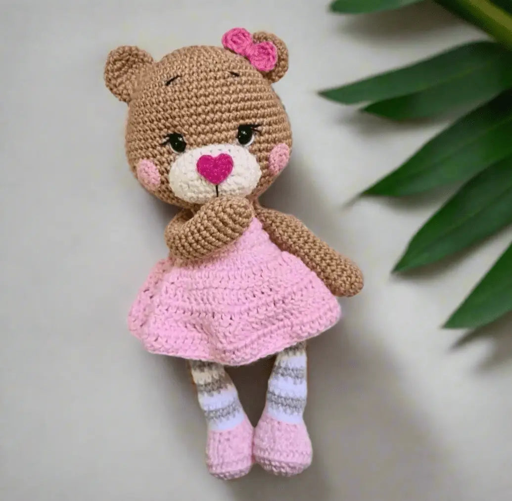 Crocheted teddy bear in pink dress with bow, heart nose, and striped socks