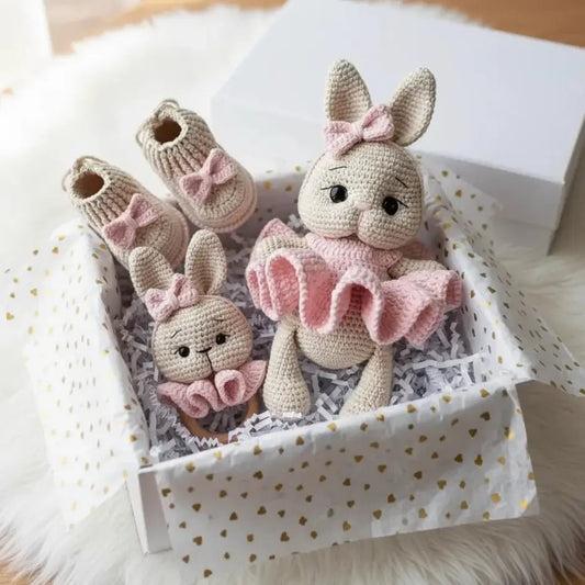 Crocheted baby bunnies and booties in pink and beige, nestled in a heart-patterned gift box.
