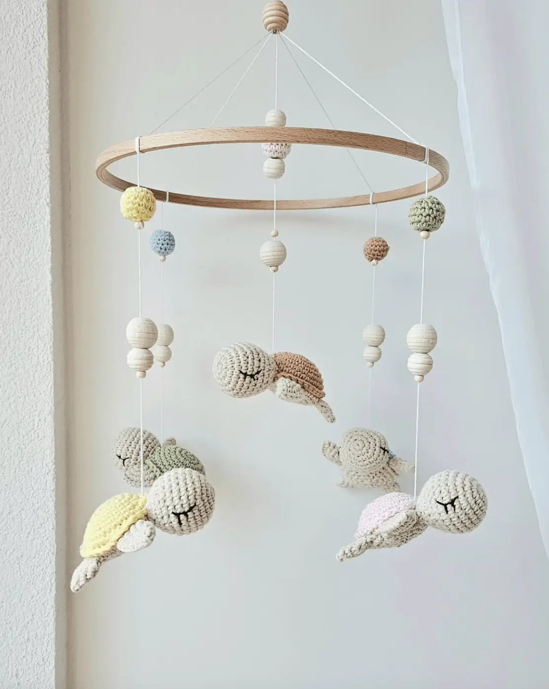 Crocheted whale and ball mobile hanging from wooden ring against white wall