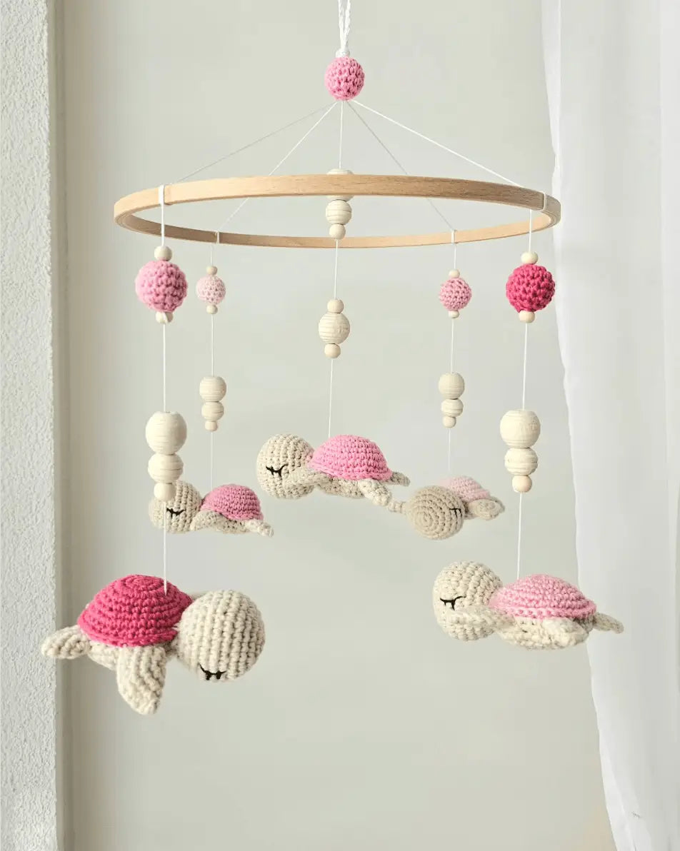 Crocheted baby mobile with sleeping pink and cream turtles hanging from wooden ring