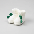 White knitted baby booties with green leaf decorations held in a hand
