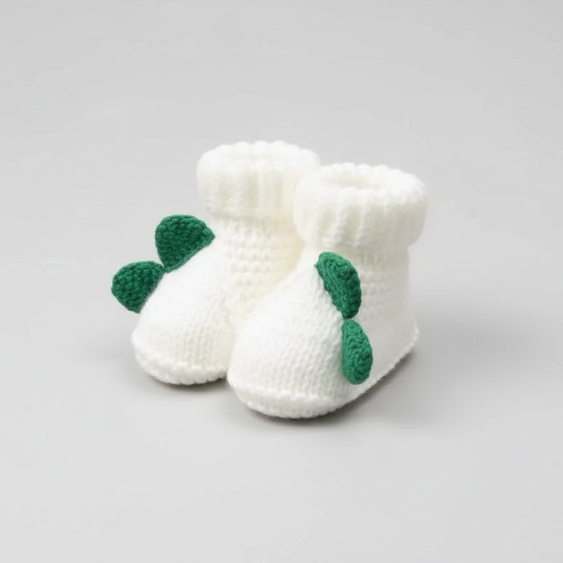 White knitted baby booties with green leaf decorations held in a hand