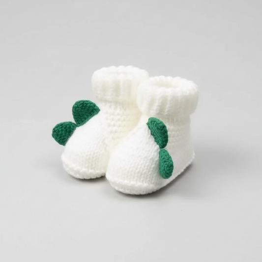 White knitted baby booties with green leaf decorations held in a hand