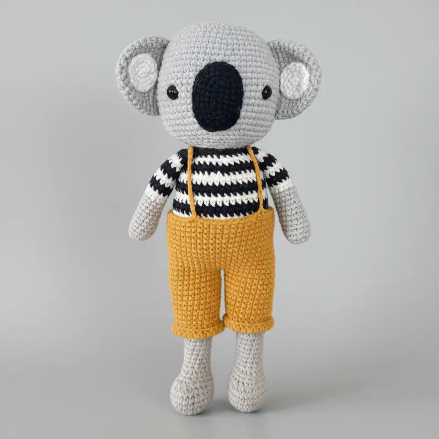 Crocheted koala wearing black and white striped shirt and yellow overalls